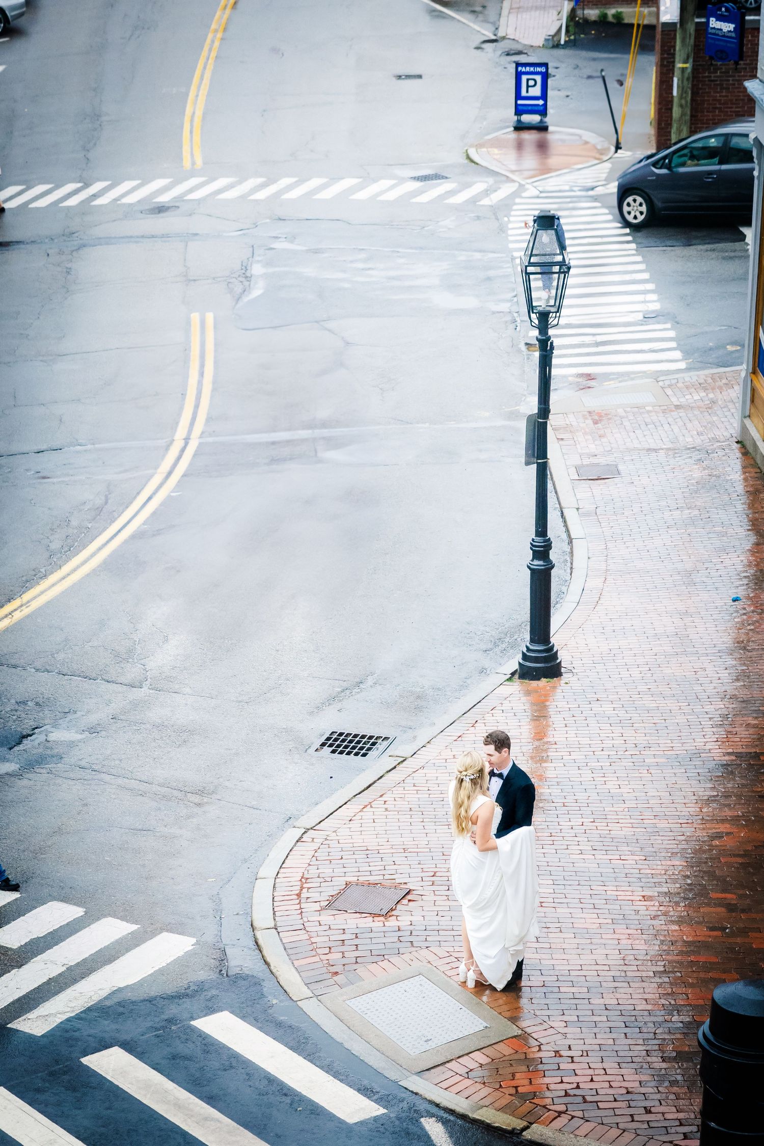 Aerial view of newlyweds standing on a brick sidewalk corner next to a vintage lamppost.