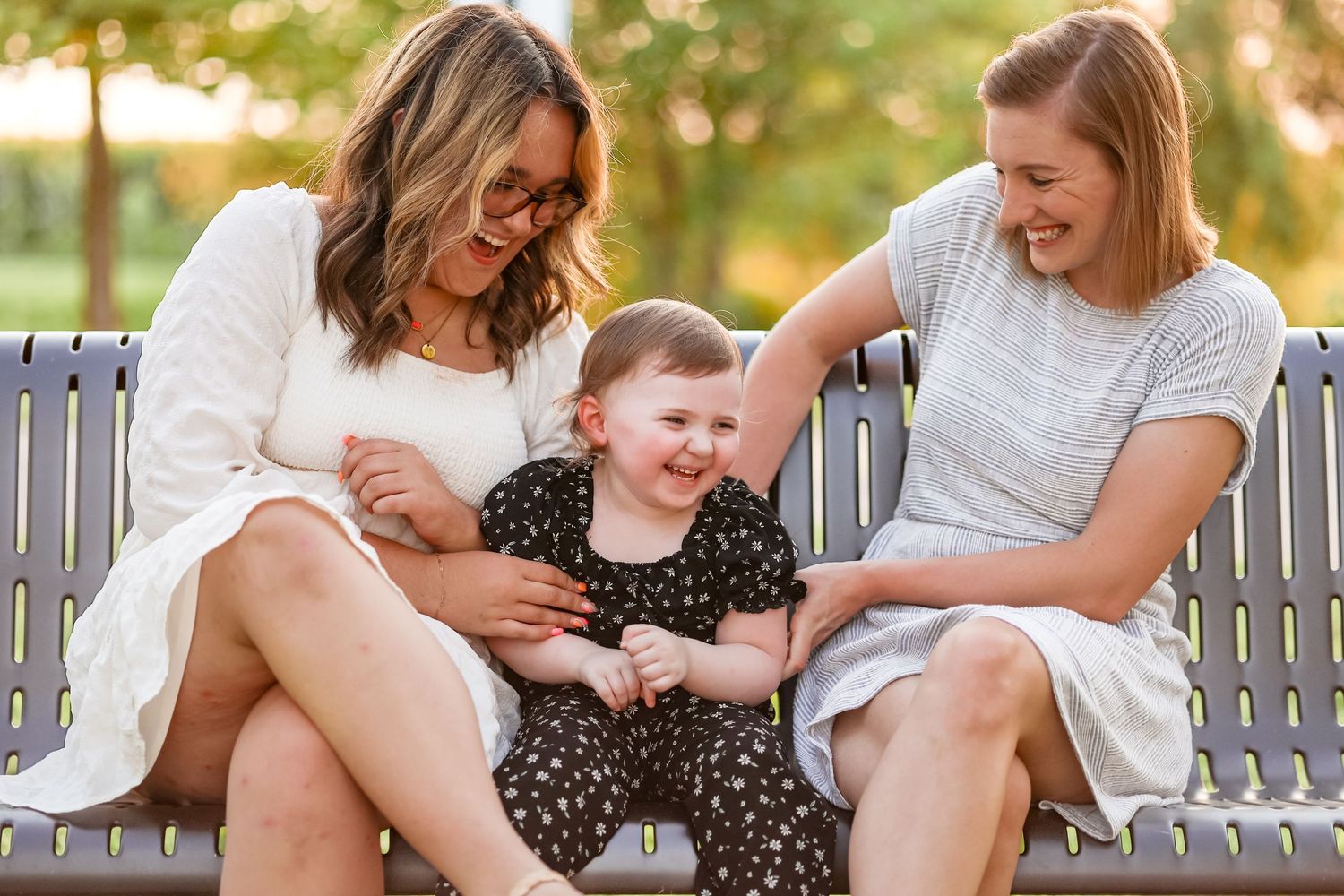 Three people sharing laughs while sitting on park bench at golden hour.
