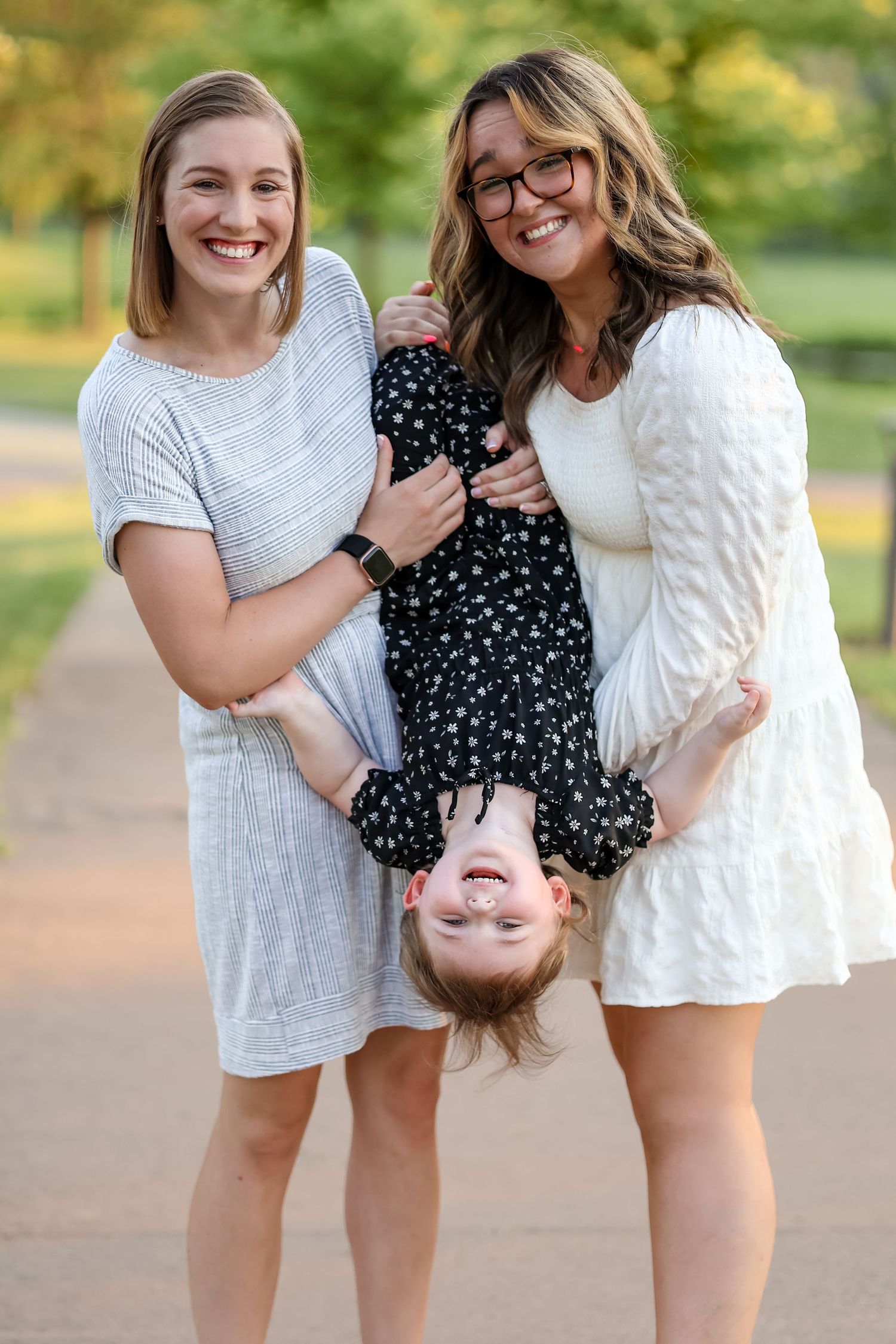 Playful family portrait with child in polka dot dress held upside down outdoors.