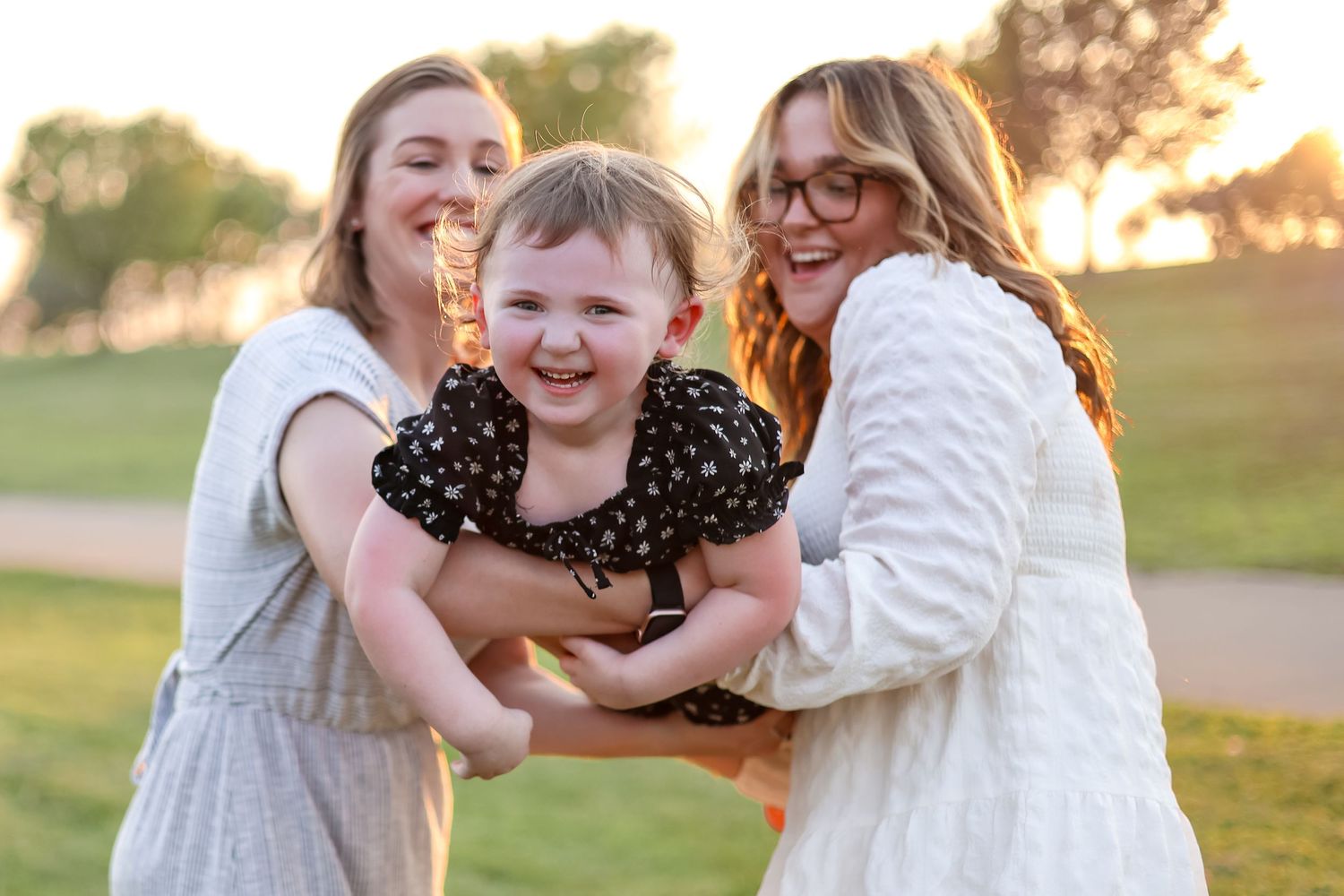 Candid moment of laughter while holding child in polka dot outfit at sunset.