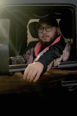 Person in glasses sitting in car interior resting against door and armrest with moody dark lighting effect.