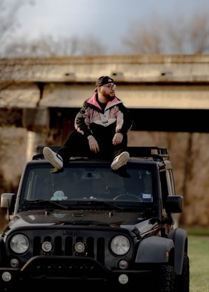 Person in casual attire lounging on the hood of a black SUV during daytime.
