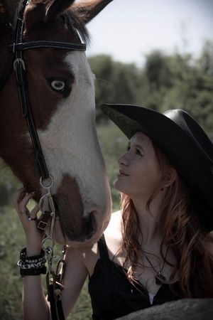A rider wearing a black cowboy hat gazes lovingly at their brown and white horse in a natural outdoor setting.