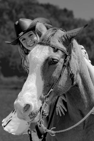 A black and white photo shows a horse with a light colored face and bridle looking at the camera from the side.