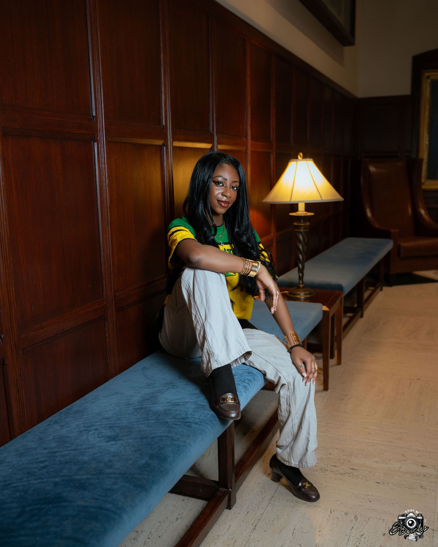 A person in green lies down precariously across a wooden table underneath a portrait in a formal dining room.