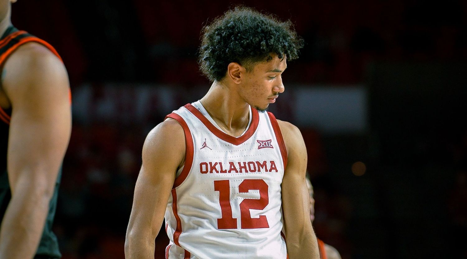 Oklahoma basketball player in white jersey number 12 intensely focuses during game action.