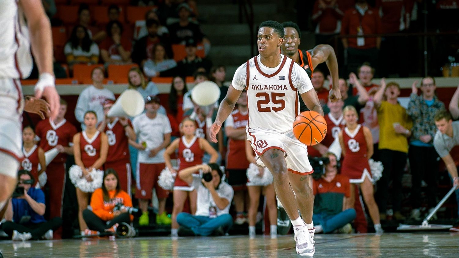 Basketball player in white Oklahoma uniform number 25 dribbles ball during game.