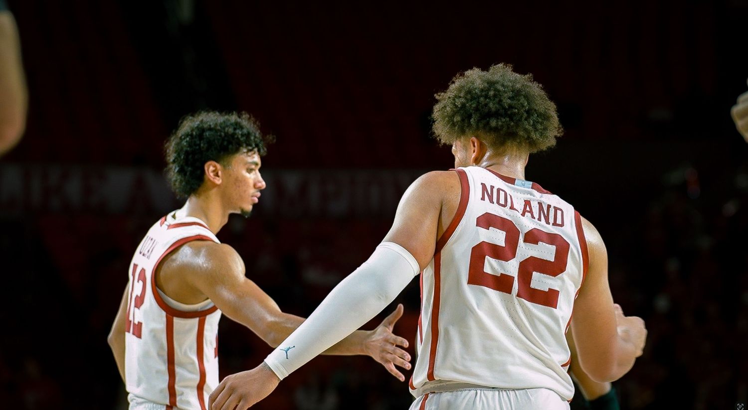 College basketball game with players in red and white uniforms on the court.