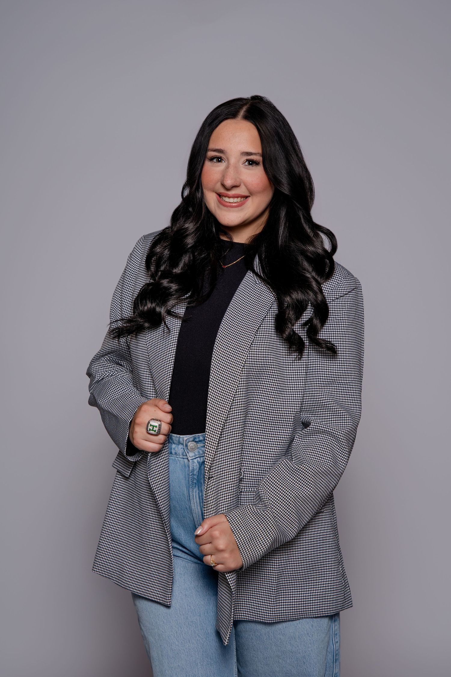 A dancer wearing a checkered blazer and jeans poses stylishly against a gray studio backdrop.