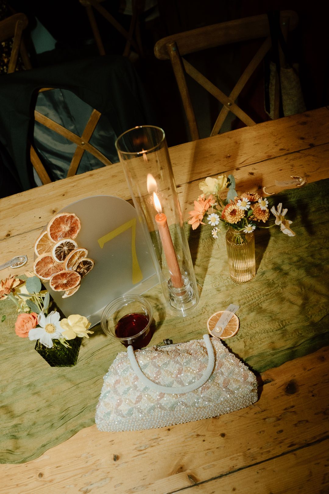 Wedding cake and delicate floral arrangements with roses and twigs on wooden table in rustic reception setting.