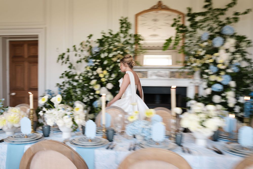 Elegant wedding reception table with blue and white floral centerpieces and fine china place settings.