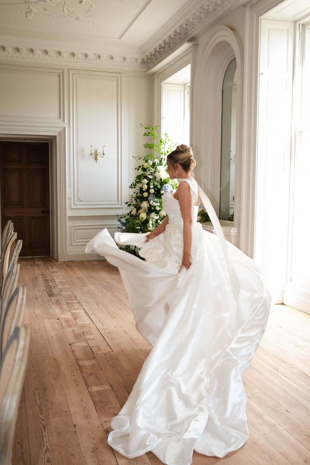 White gown twirling in an elegant room with ornate moldings and hardwood floors.