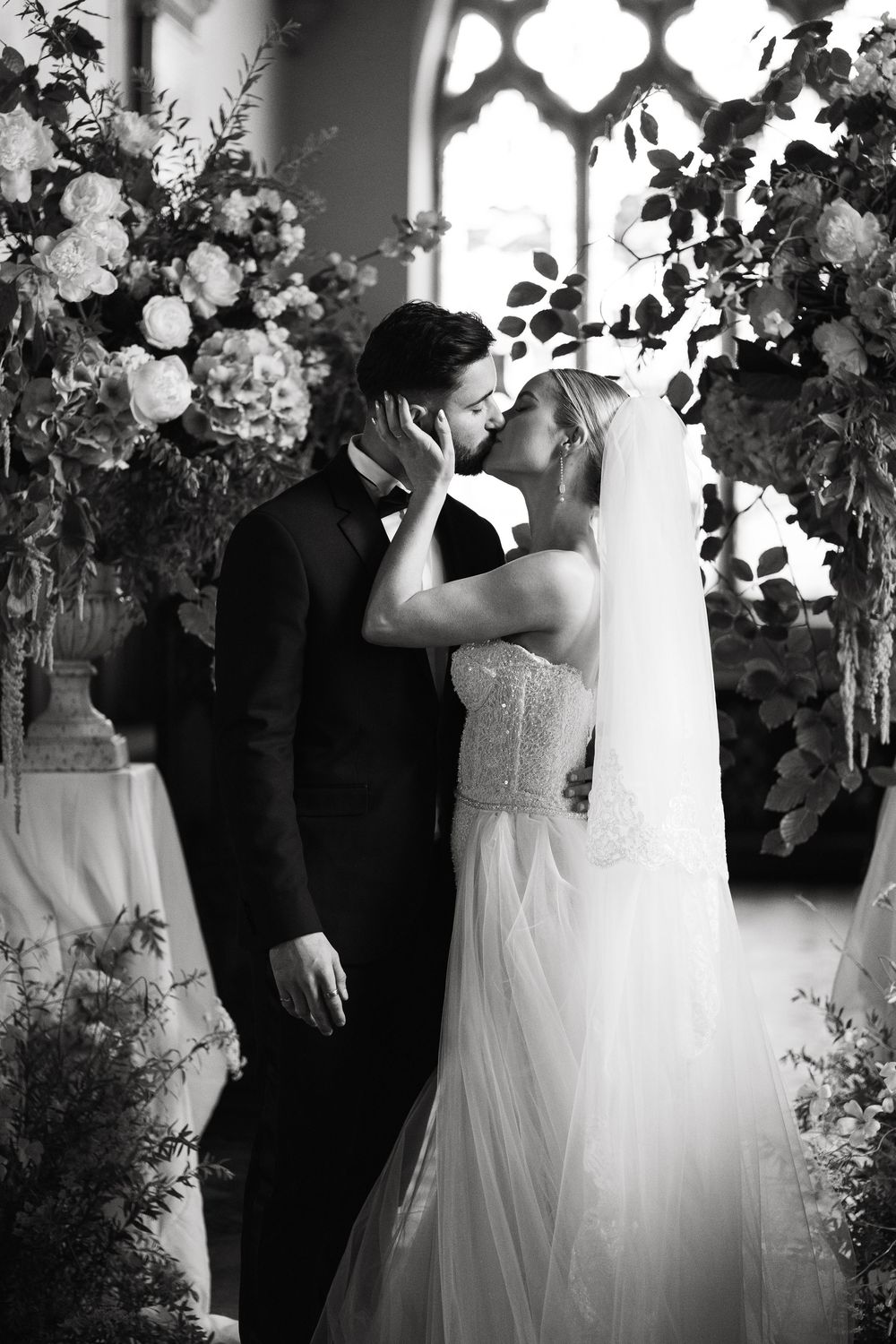 Black and white wedding portrait with dramatic lighting and floral archway decorations.
