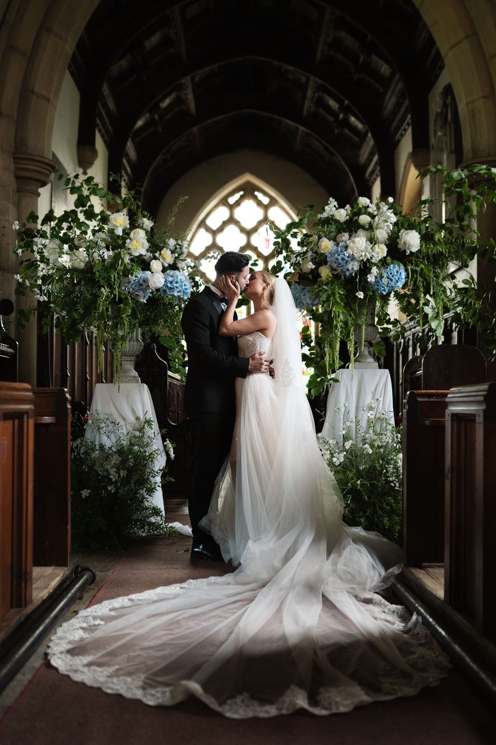 Wedding couple posing in Gothic-style corridor decorated with white flowers and greenery.