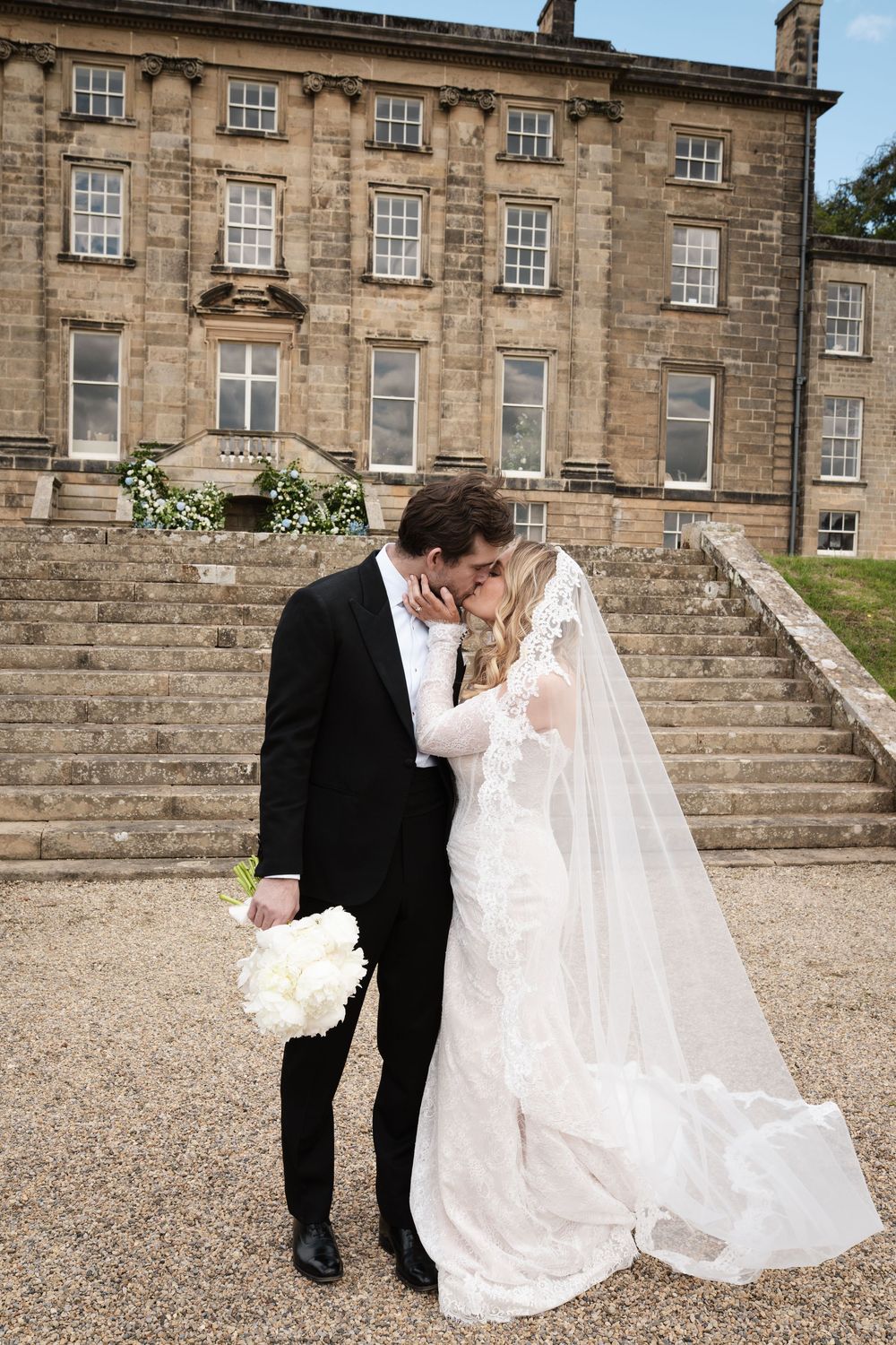 A wedding couple shares an intimate moment on stone steps of a grand historic mansion.