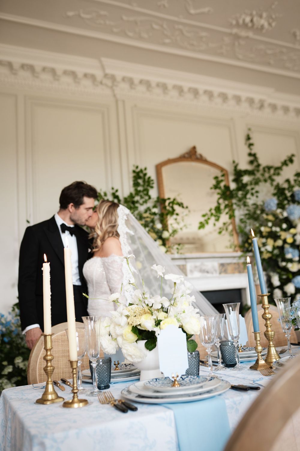 Newlyweds embrace at an elegant table setting with blue and white floral decor.