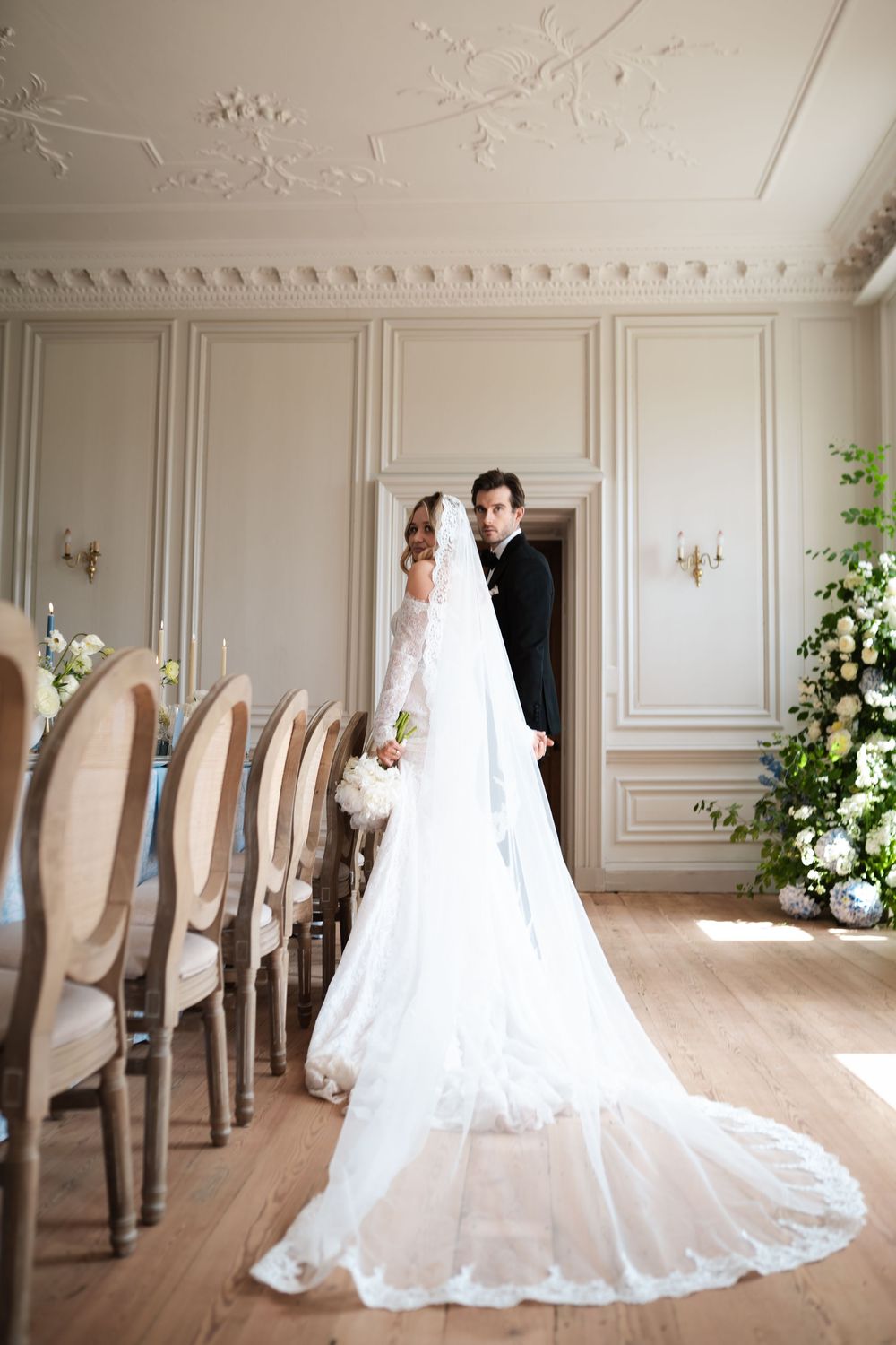 A wedding couple poses in an ornate room with a flowing white dress and elegant decor.