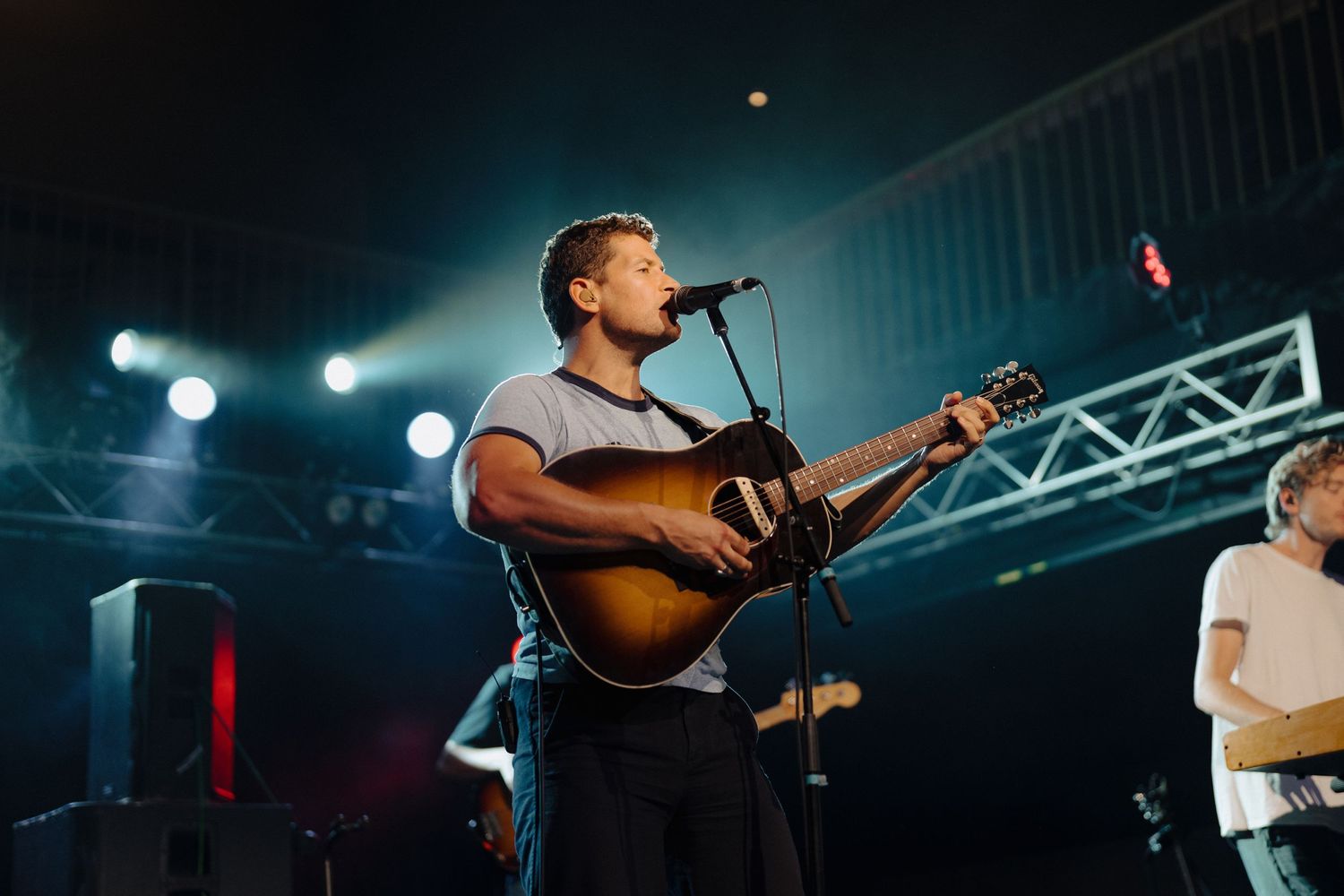 A musician performs on stage with an acoustic guitar under dramatic concert lighting.
