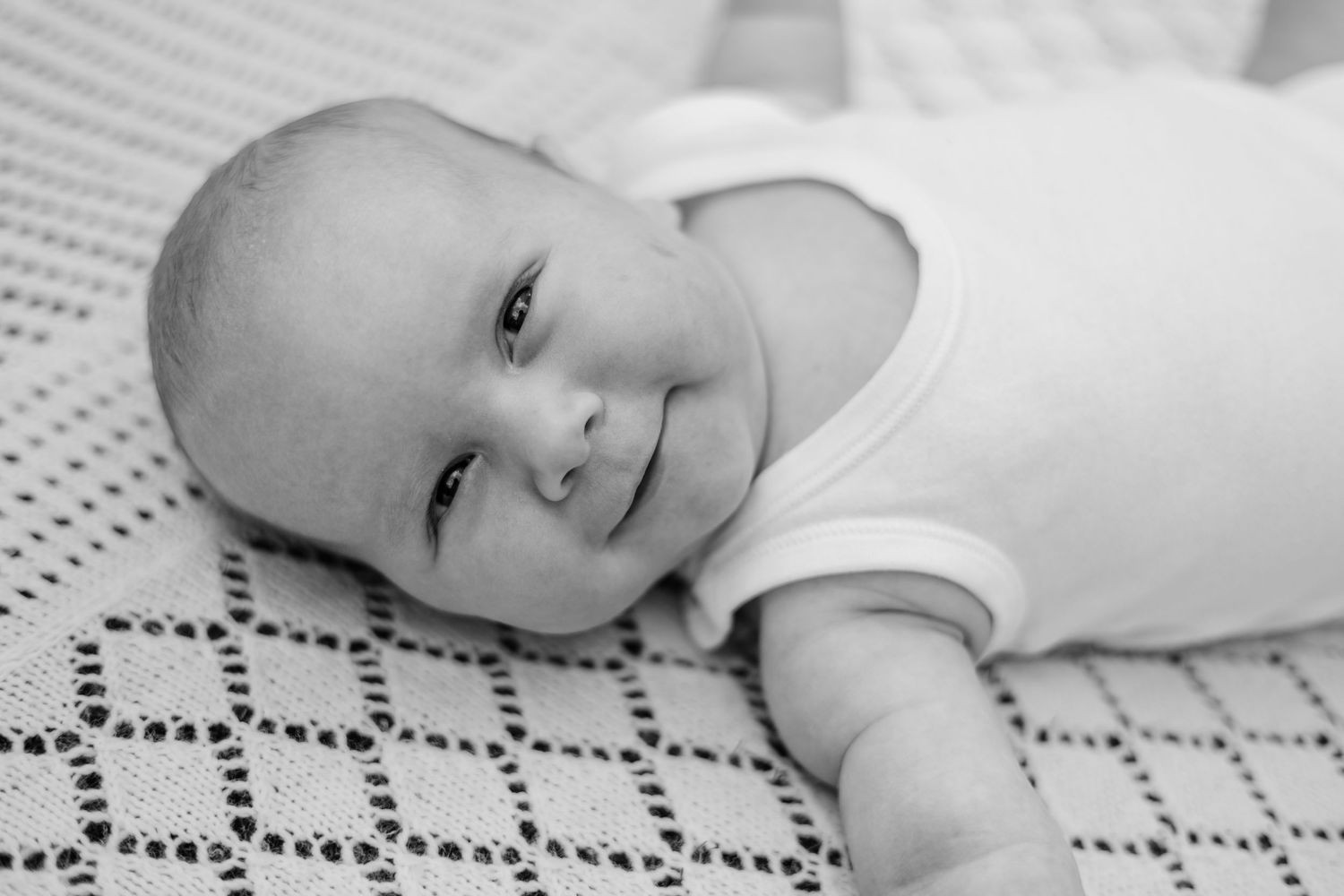 In-home photoshoot with baby laying on the grass in a white vest, on a white blanket, in Balham, London
