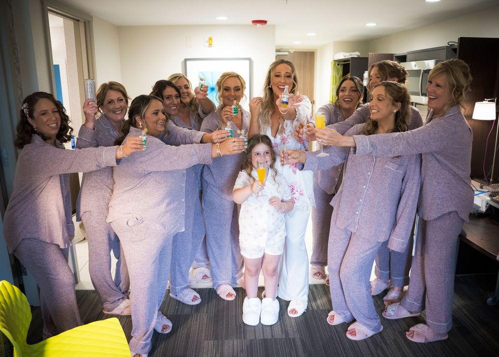 A wedding party wearing matching lavender suits and dresses raises their glasses in celebration at an indoor venue.