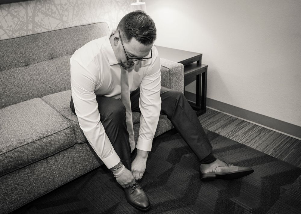 Person in dress clothes sits on gray carpeted stairs with hand resting on neck in black and white photograph.