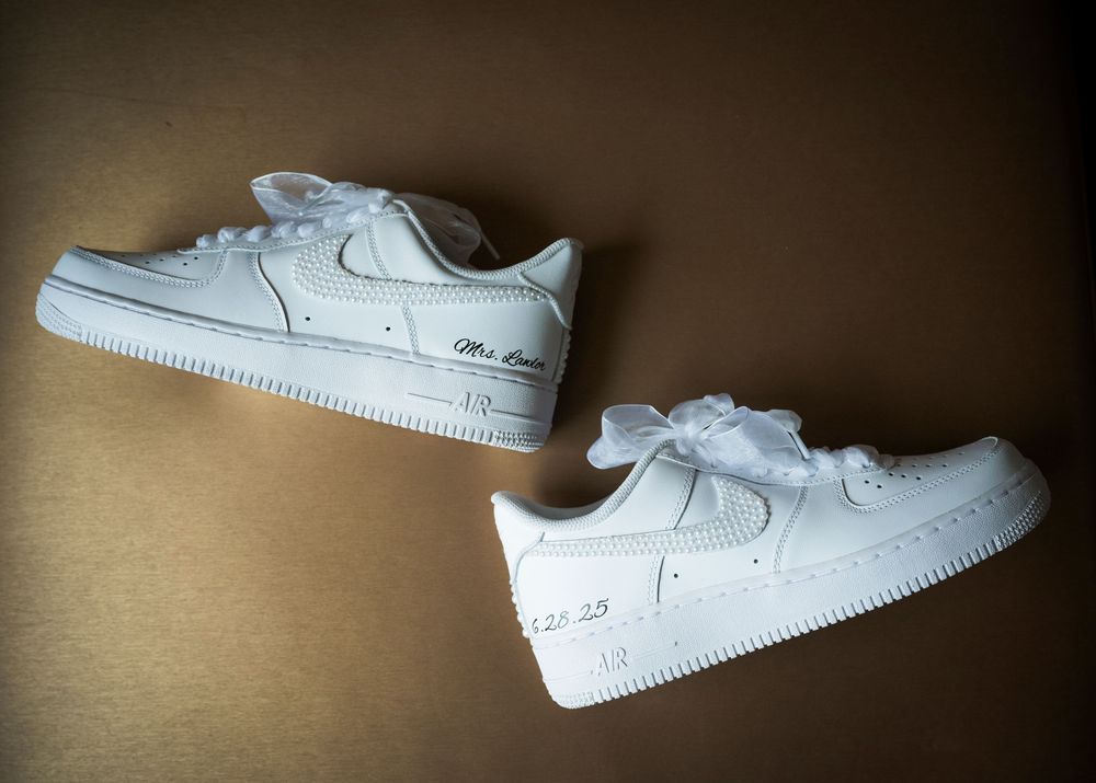 A pair of white Nike Air Force 1 Low sneakers displayed against a brown background.