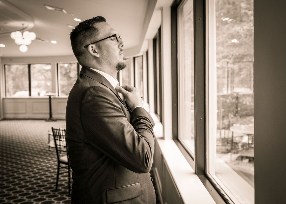 A thoughtful businessman in a gray suit gazes out large windows in an elegant hallway with chandelier lighting.