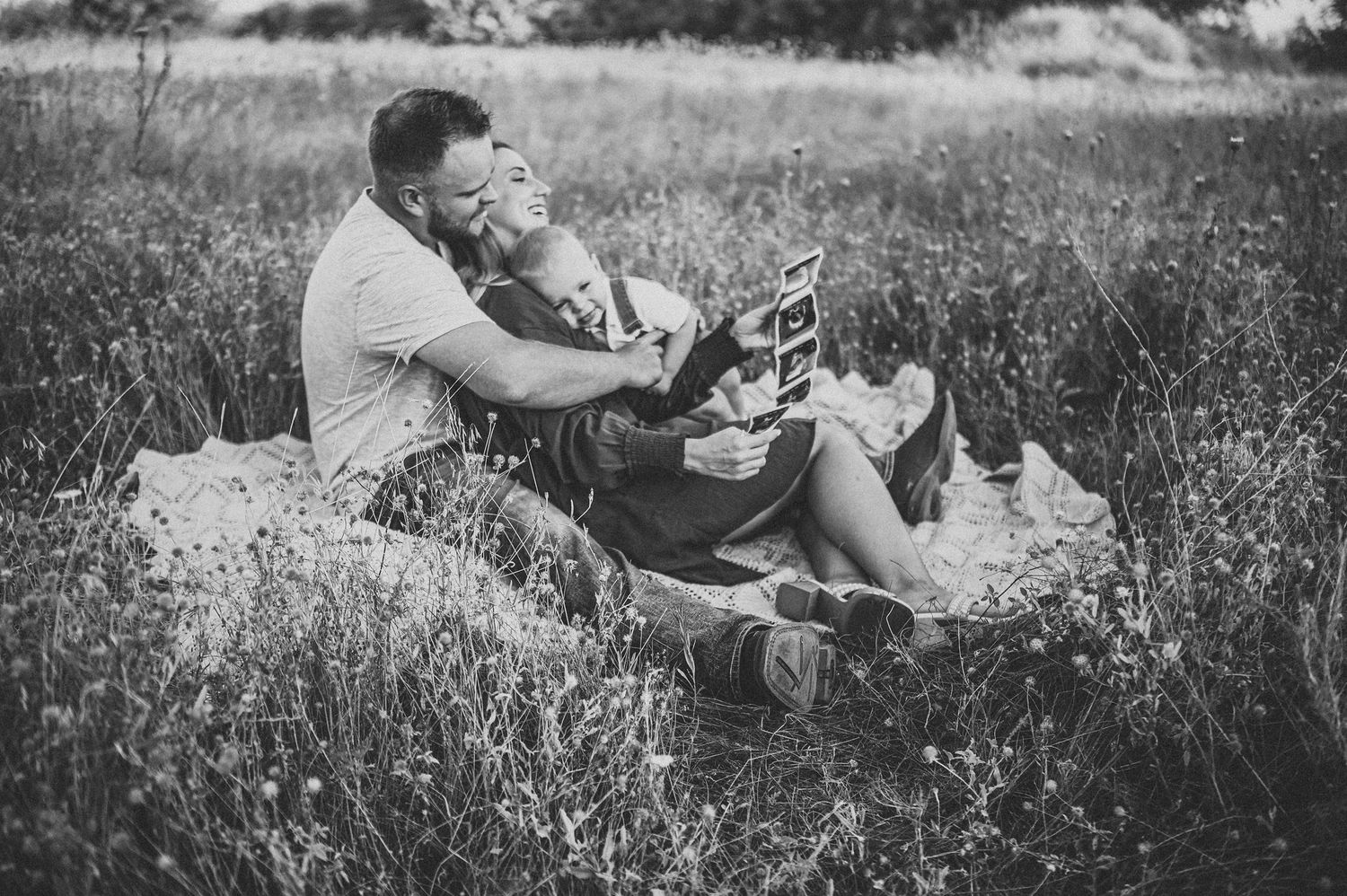 Black and white photo of a couple sitting in a meadow, sharing a tender moment while looking at a book.