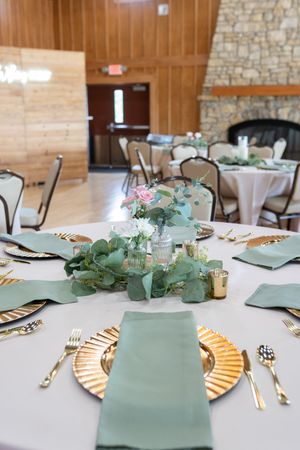 Reception tables decorated with sage green napkins, gold chargers, and eucalyptus centerpieces.