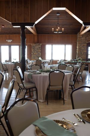 Rustic wedding reception venue with wooden beams, stone walls, and round tables set with white linens and mint accents.