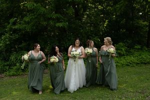 Wedding party arranged in casual poses on grass with bridesmaids in sage green dresses.