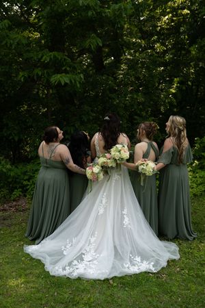 Wedding party shown from behind with bridesmaids in sage dresses and bride in flowing white gown.