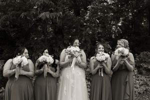Wedding party poses with bouquets against natural backdrop in black and white photography.