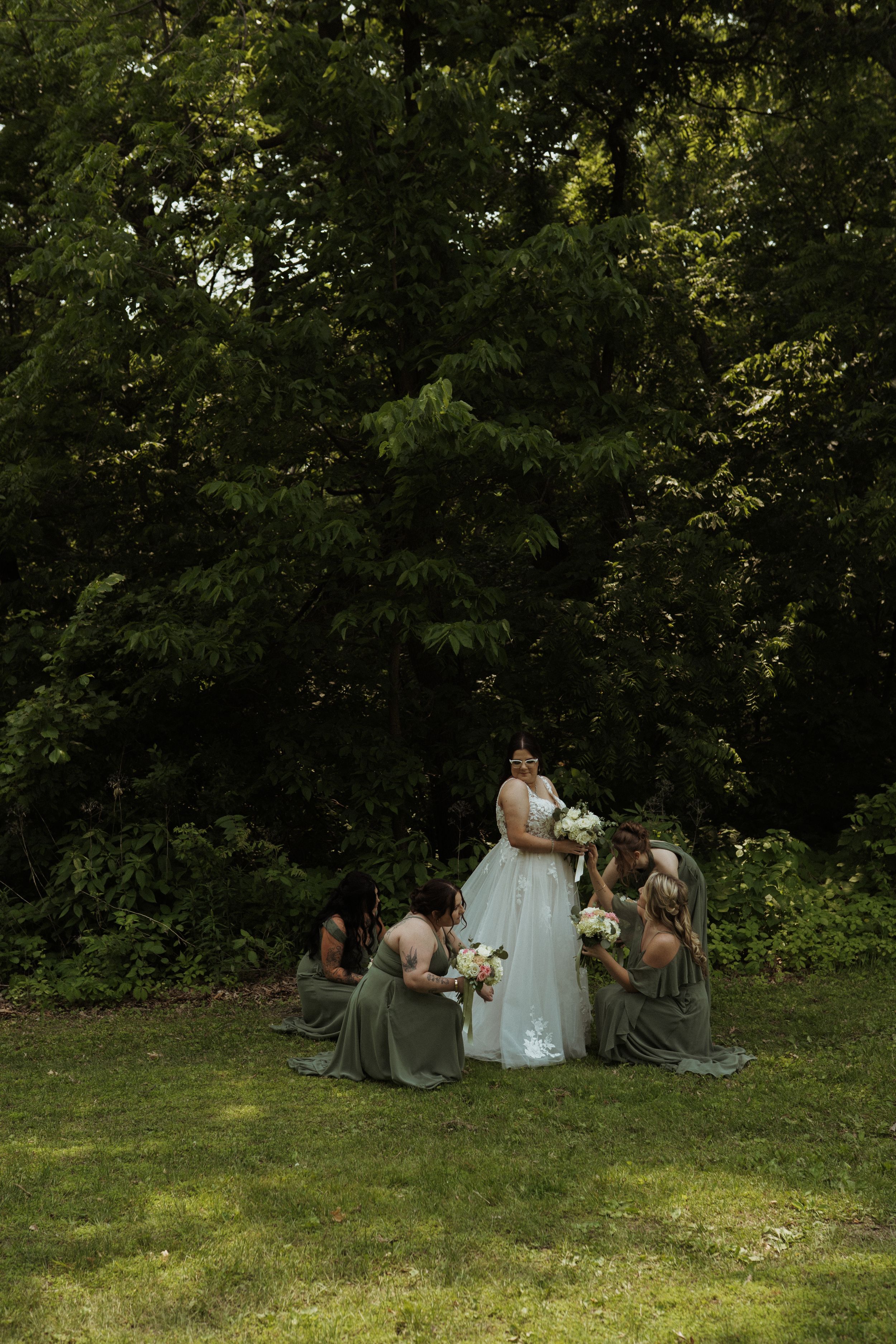 Wedding party gathered on a grassy hill surrounded by lush green trees.