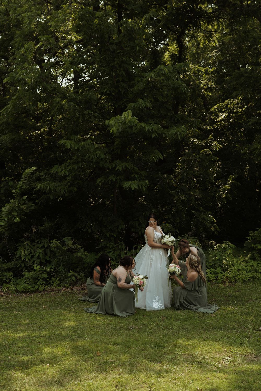 Wedding party gathered on a grassy hill surrounded by lush green trees.