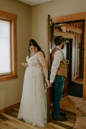A couple shares an intimate first look moment in a hallway before their wedding ceremony.