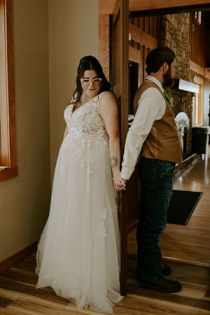 A couple in wedding attire shares a tender moment in a sunlit indoor hallway.