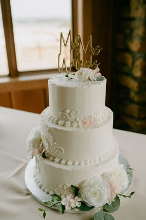 Elegant white wedding cake with delicate floral decorations and metallic cake topper.
