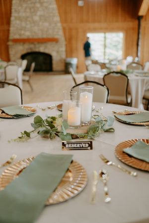 Wedding reception table settings with sage green napkins and gold charger plates.