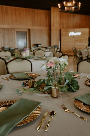 Elegant wedding reception table with gold chargers and sage green napkins.