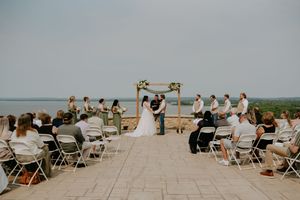 Panoramic view of an outdoor wedding ceremony with guests seated on white chairs.