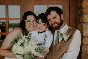 Wedding party poses together in rustic brick venue with white floral arrangements.