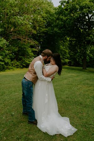 Romantic wedding dip pose photographed in a scenic green garden setting.
