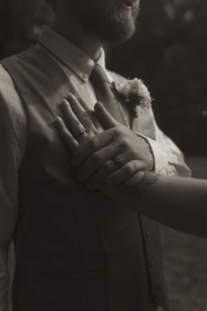Black and white artistic shot of wedding rings and hands with dramatic shadows.