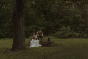 Wide landscape shot of wedding couple sitting on wooden bench in peaceful forest setting.