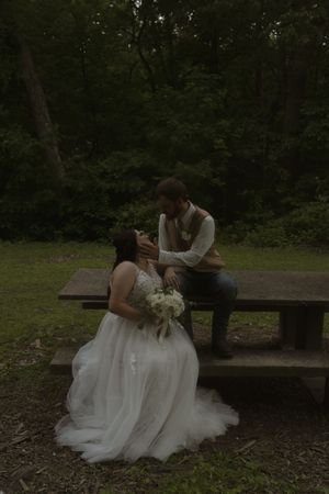 Wedding couple sharing intimate moment on rustic park bench surrounded by greenery.