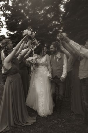 Wedding party in gray dresses and tan vests celebrating outdoors with raised arms.