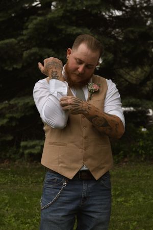 A person in a tan vest holds a small baby at an outdoor gathering.