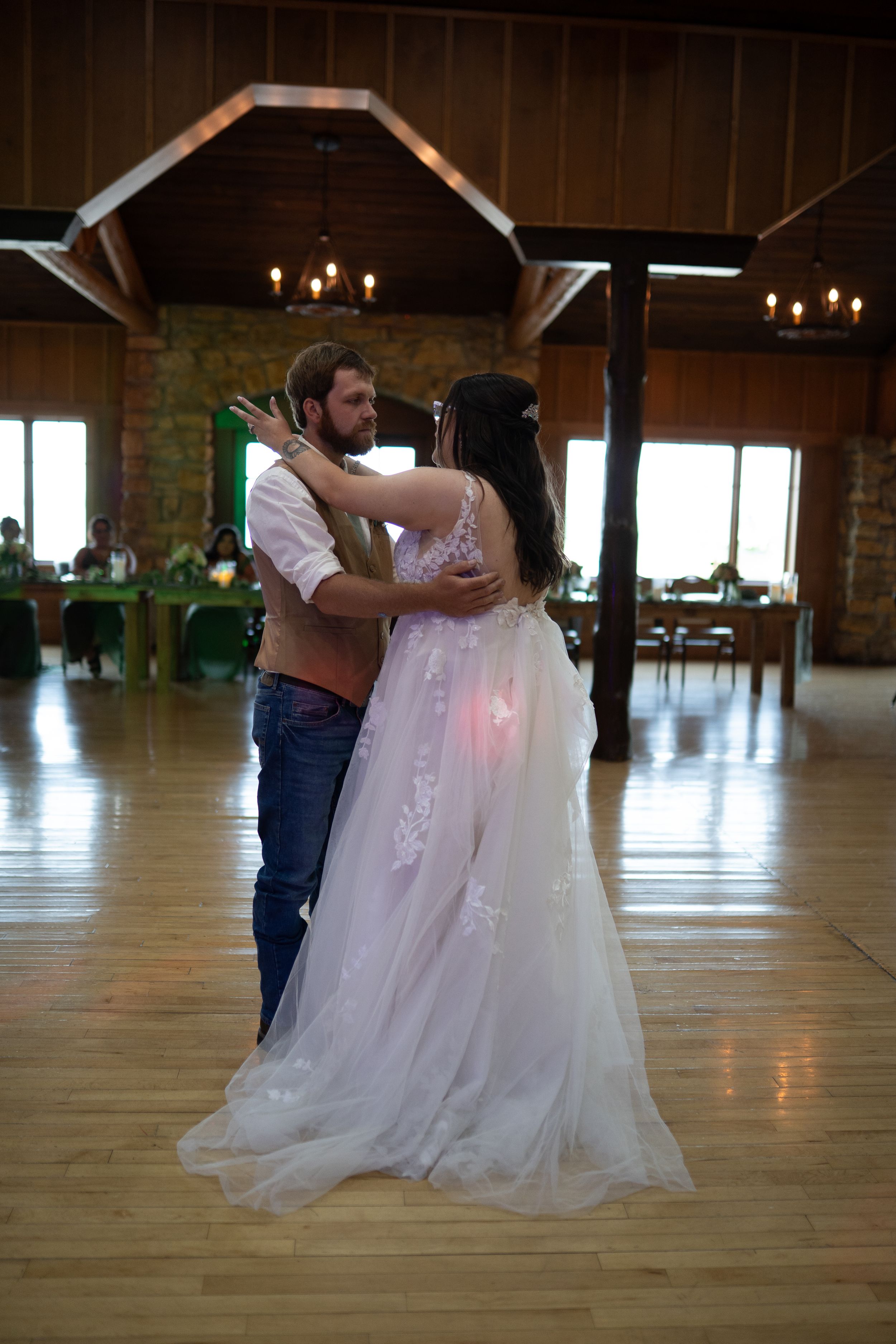 Romantic dance moment in rustic reception hall with wooden beams and natural window light.