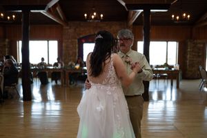 Couple sharing their first dance in rustic venue with wooden beams and natural lighting.